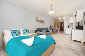 Ein modernes Hotelzimmer mit Bett, einer Sitzecke, einem Schreibtisch und einer Küchenzeile.