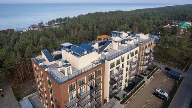 A multi-story residential building with balconies, a parking area, and a view of the sea. - Bright apartment with balcony | Right on the beach in Miedzywodzie (Międzywodzie)