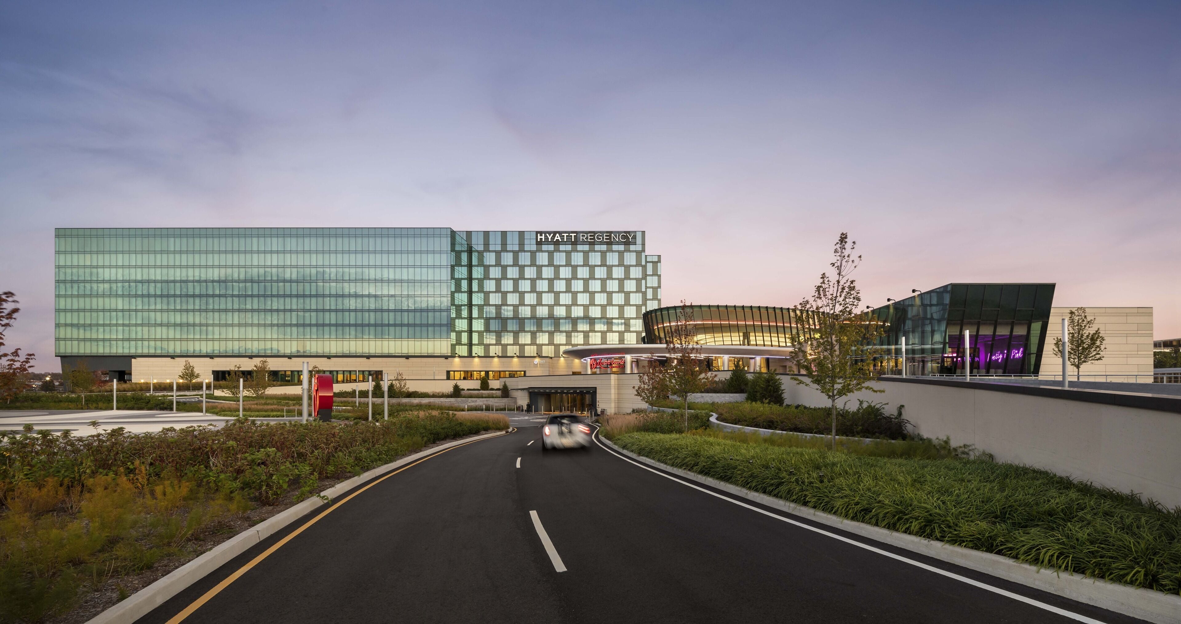 A modern hotel with a glass facade, a curved entrance, and a landscaped area with trees.