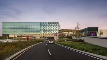 A modern hotel with a glass facade, a curved entrance, and a landscaped area with trees.