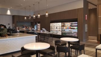 A modern cafe with a bar area, seating, and a refrigerated display of beverages.