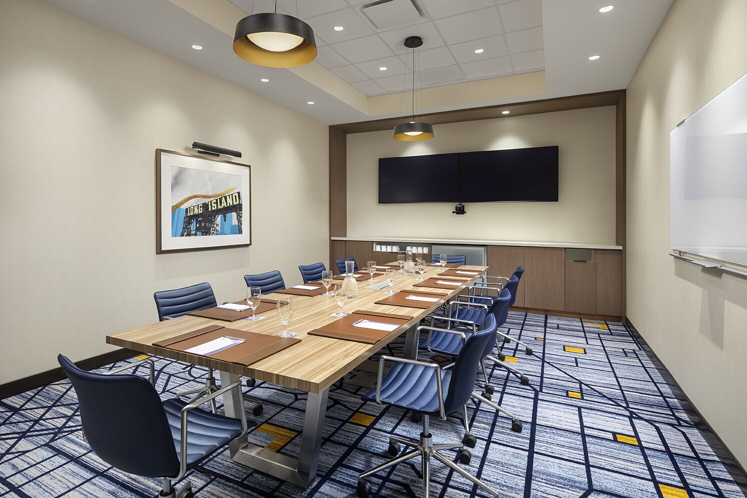 A conference room with a long table, blue chairs, and a large screen on the wall.