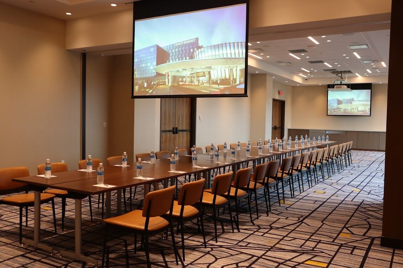 A conference room with a long table, chairs, and a large screen displaying a building image.