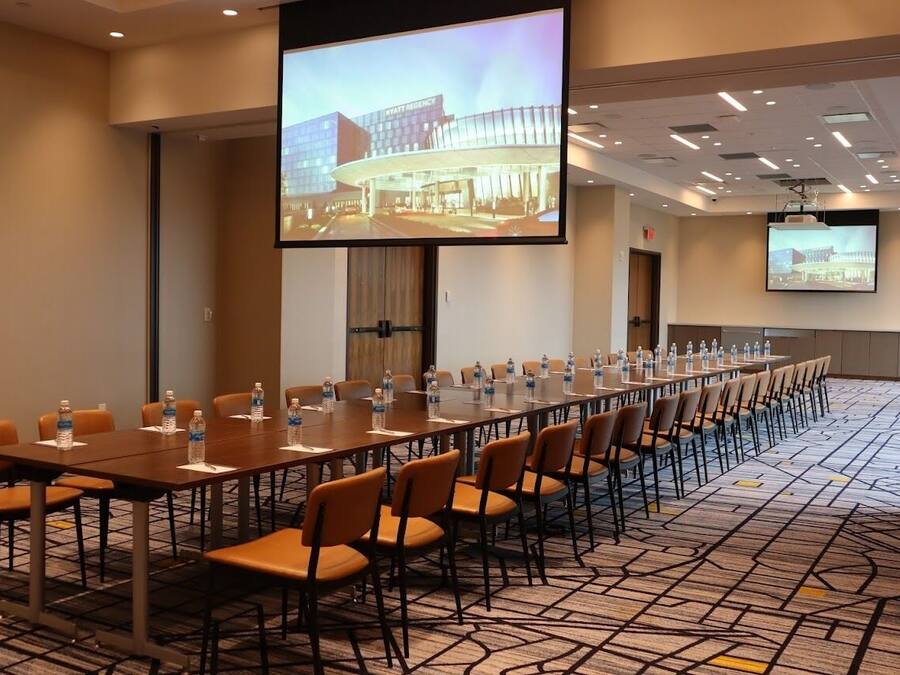 A conference room with a long table, chairs, and a large screen displaying a building image.