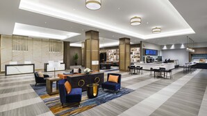 A modern hotel lobby with a reception desk, seating area, and a bar.