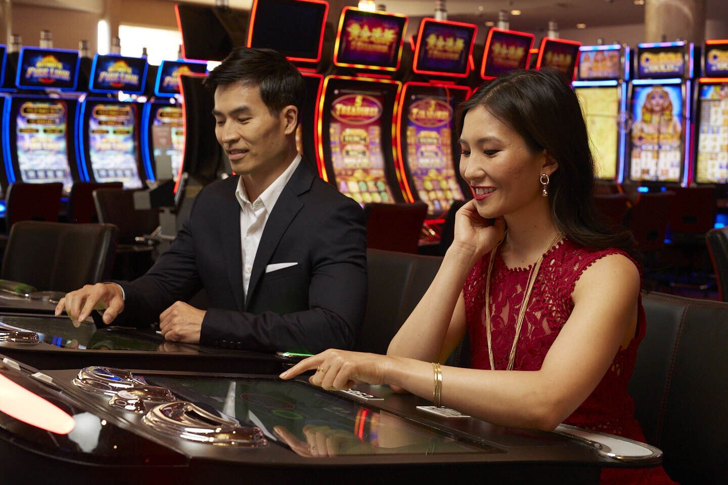 Un casino con varias máquinas tragamonedas y un hombre y una mujer jugando en una mesa.