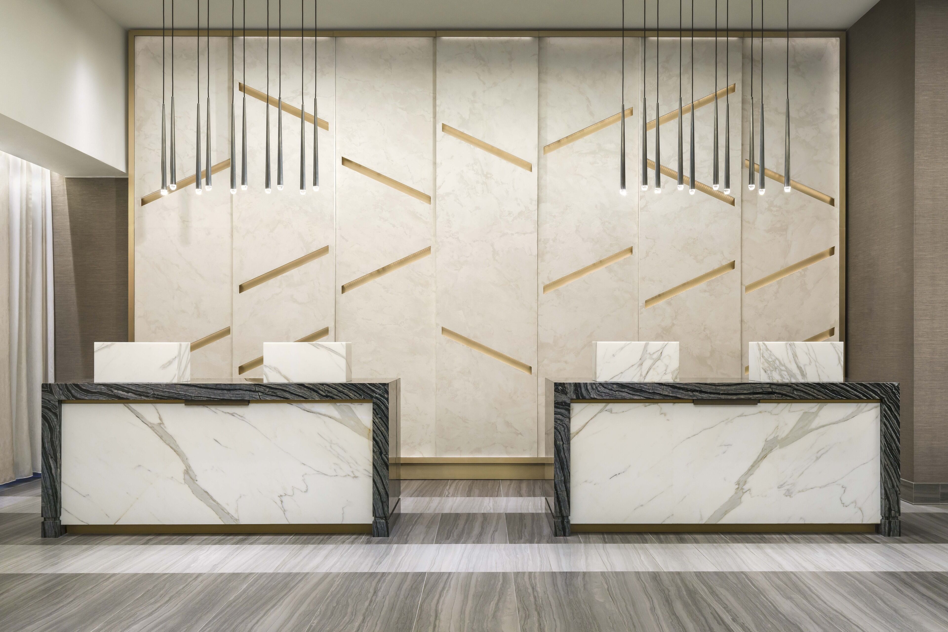 A reception area with marble counters, a modern chandelier, and a geometric wall design.