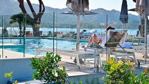 A poolside area with lounge chairs, umbrellas, and a glass barrier. - La Roya (Saint-Florent)