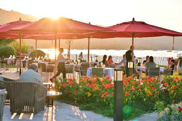 An outdoor dining area with tables and chairs, umbrellas, and a view of the water.