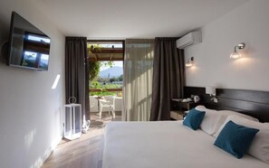 Quarto de hotel com cama, televisão na parede, mesa pequena com cadeiras e vista para o exterior.
