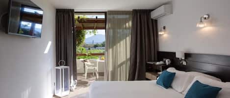A hotel room with a bed, a TV mounted on the wall, a small table with chairs, and a view of the outdoors.
