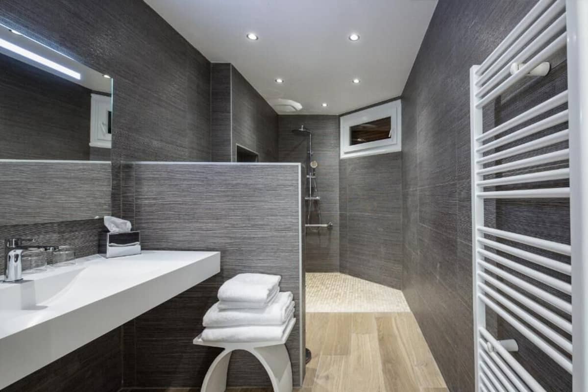 A modern bathroom with a large mirror, a white sink, a towel rack, and a shower area.