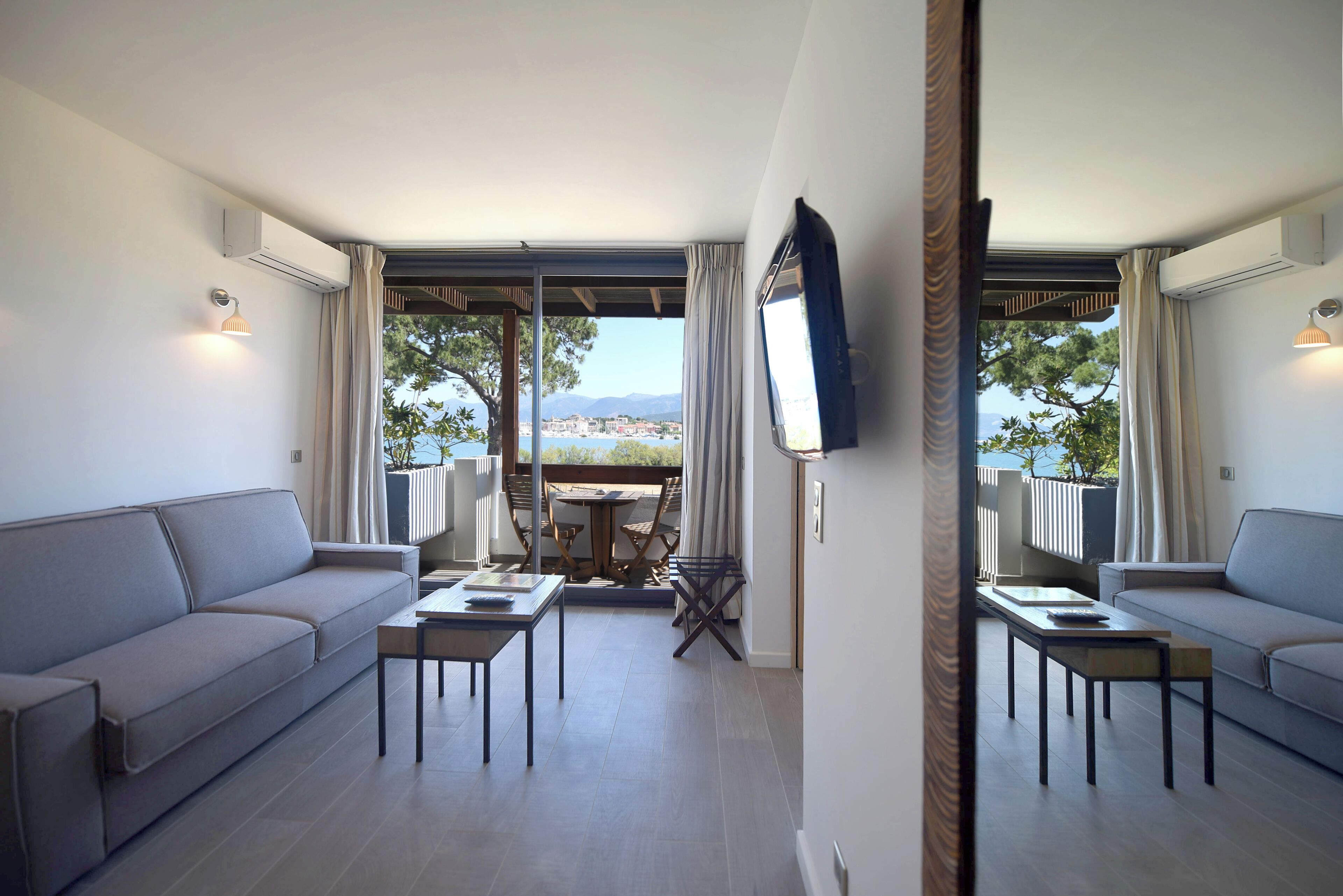 A modern living room with a sofa, two tables, a TV, and a balcony with a table and chairs.