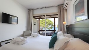 A hotel room with a bed, a TV, a window with curtains, and a view of the outdoors. - La Roya (Saint-Florent)