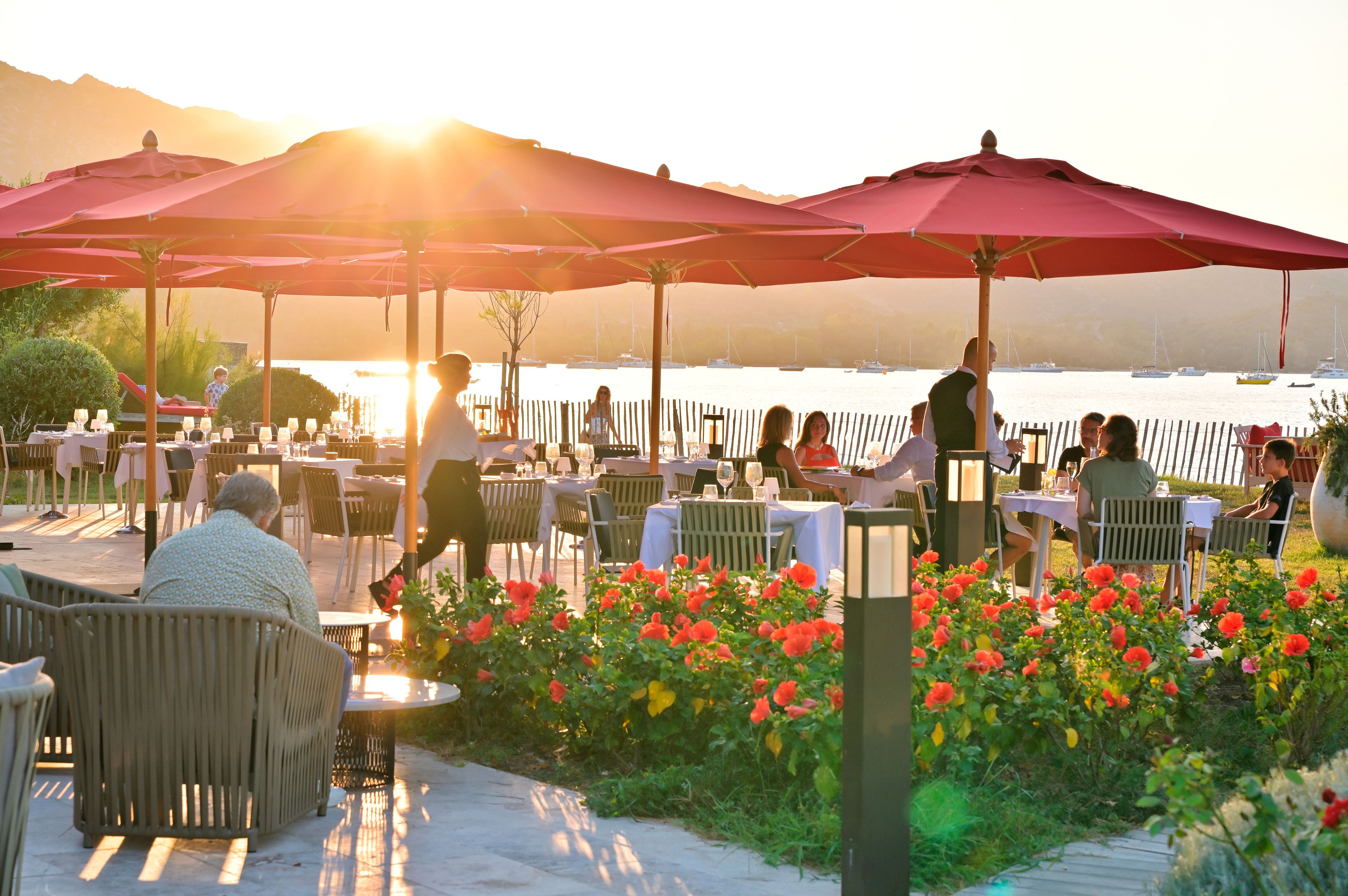 Un espace extérieur aménagé pour les repas, avec des tables, des chaises, des parasols et une vue sur l’eau.
