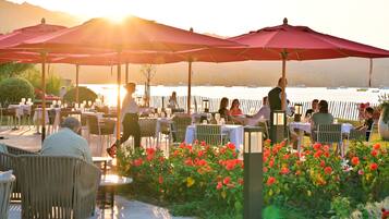 Un espace extérieur aménagé pour les repas, avec des tables, des chaises, des parasols et une vue sur l’eau.