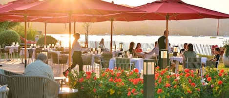 An outdoor dining area with tables and chairs, umbrellas, and a view of the water.