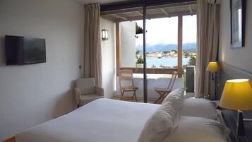 A hotel room with a bed, a TV, a chair, a table, and a view of the sea.
