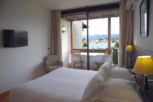 Habitación de hotel con cama, televisión, silla, mesa y vista al mar.