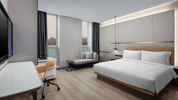 A modern hotel room with a large bed, a desk, a sofa, and a TV.