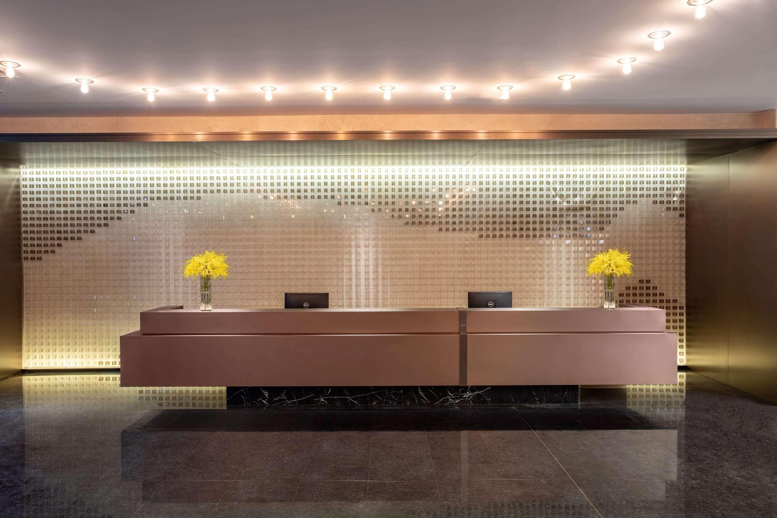 A reception area with a modern design, featuring a reception desk, two vases with yellow flowers, and a patterned wall.