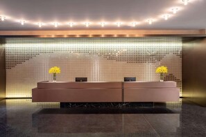 Uma área de recepção com design moderno, com balcão de atendimento, dois vasos com flores amarelas e um painel de parede trabalhado.
