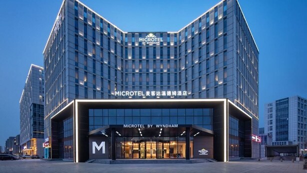 Um hotel Microtel moderno, com entrada destacada e céu claro ao fundo.
