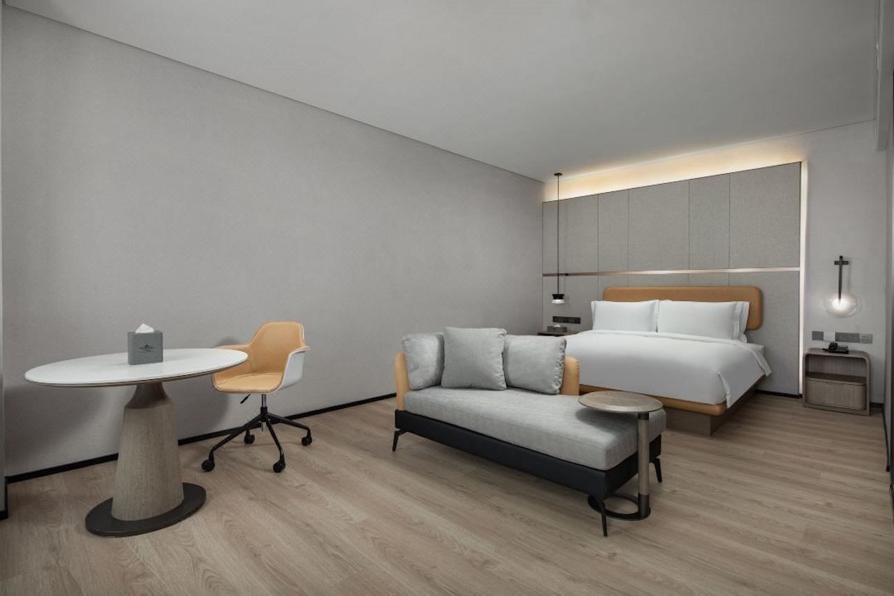 A modern hotel room with a bed, a sofa, a small table, and a chair.