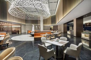 Um lobby de hotel moderno com área de estar central, bar e balcão de recepção.