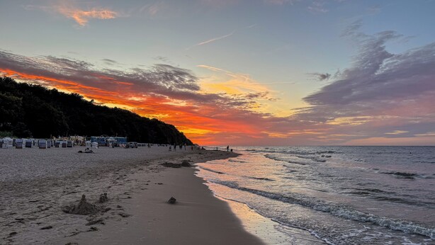 Une plage avec un coucher de soleil, un rivage sablonneux et des parasols de plage.