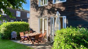 Une maison en bois avec une table et des chaises sur une terrasse, entourée de verdure.