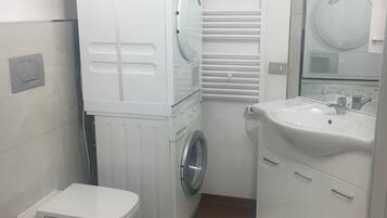 Un baño pequeño con inodoro, lavadora y lavamanos.