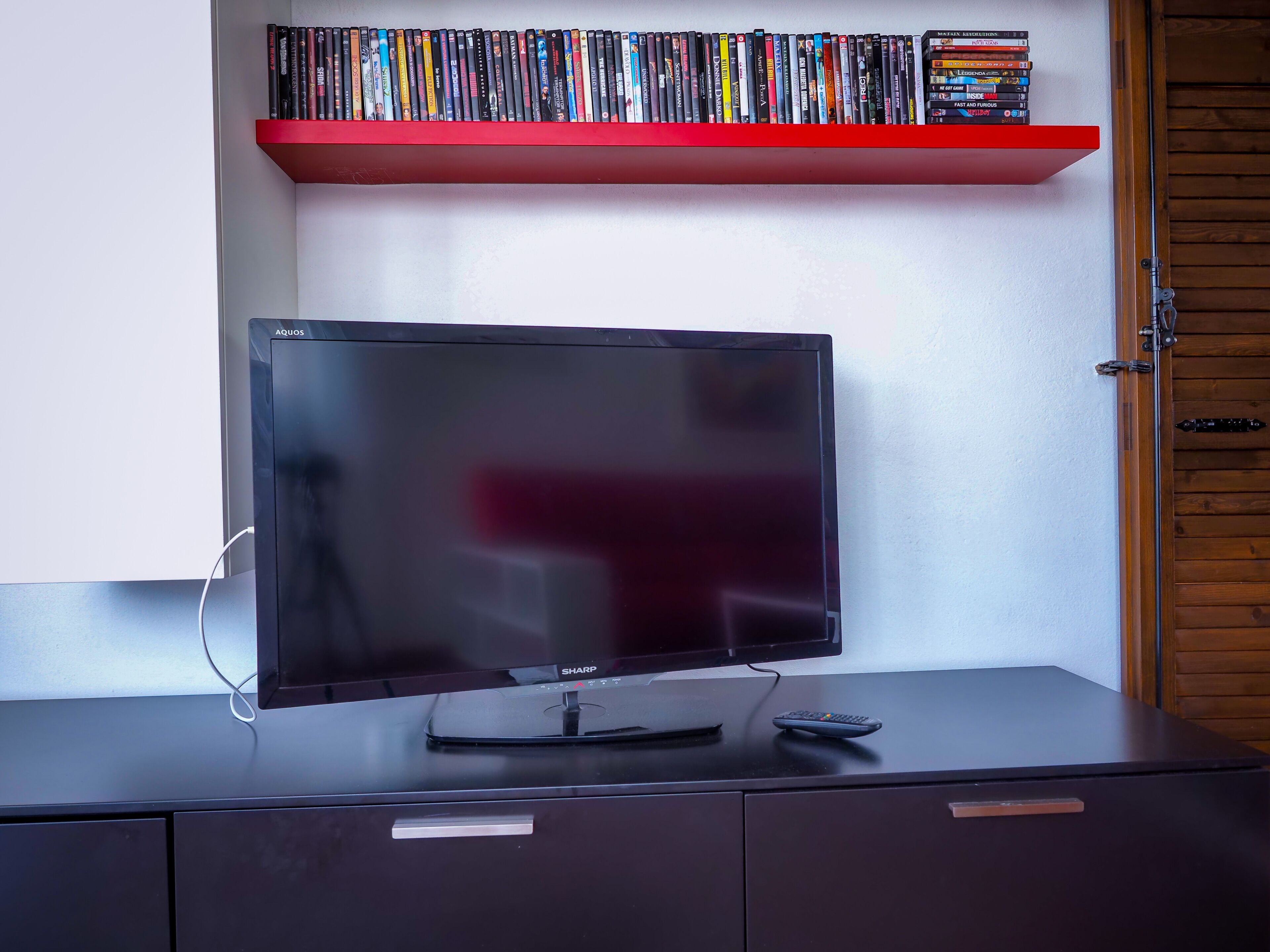 Un televisor sobre un mueble negro con un estante rojo donde hay DVDs.