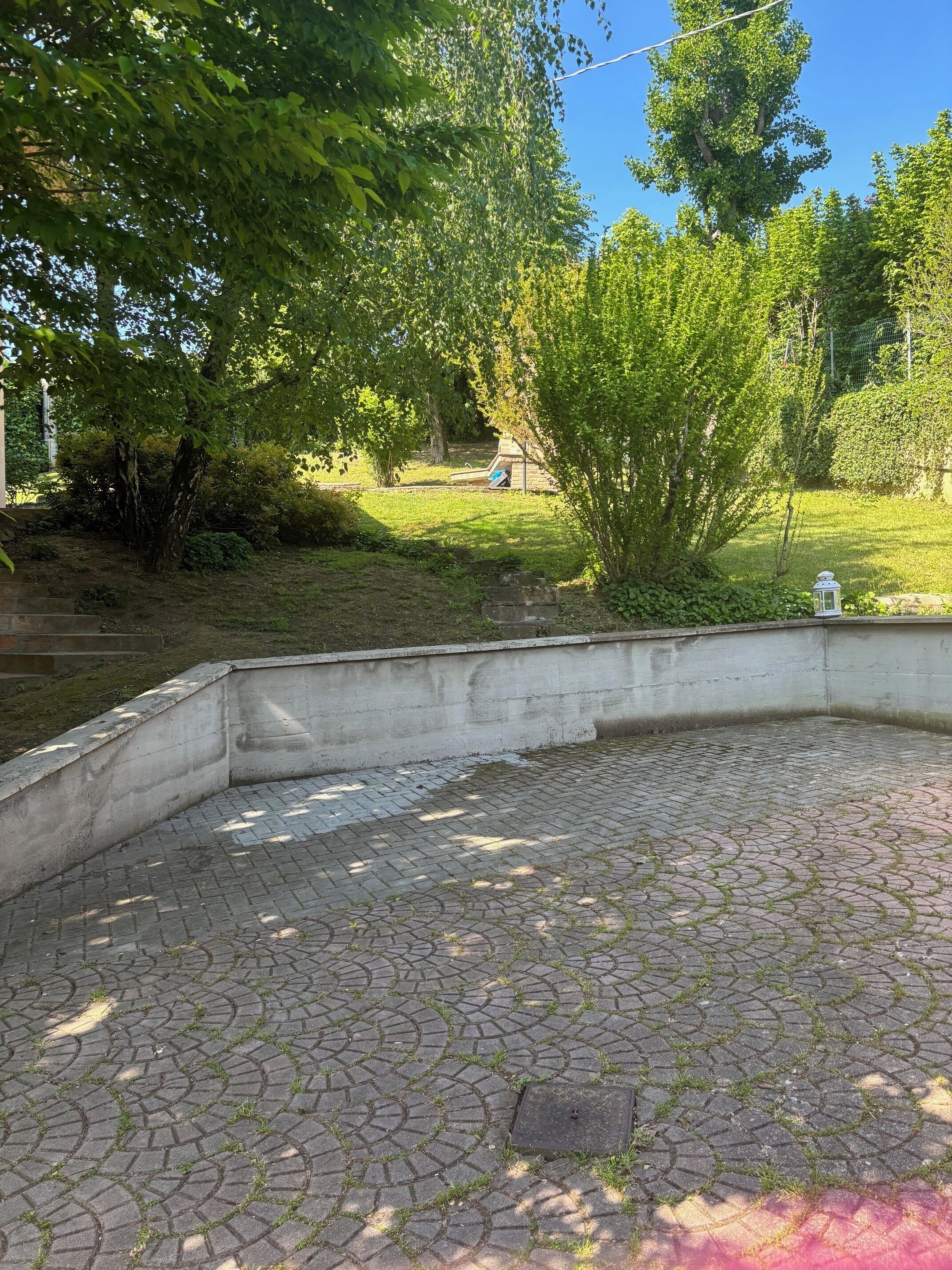 Un patio empedrado con un muro de hormigón, rodeado de árboles y vegetación.