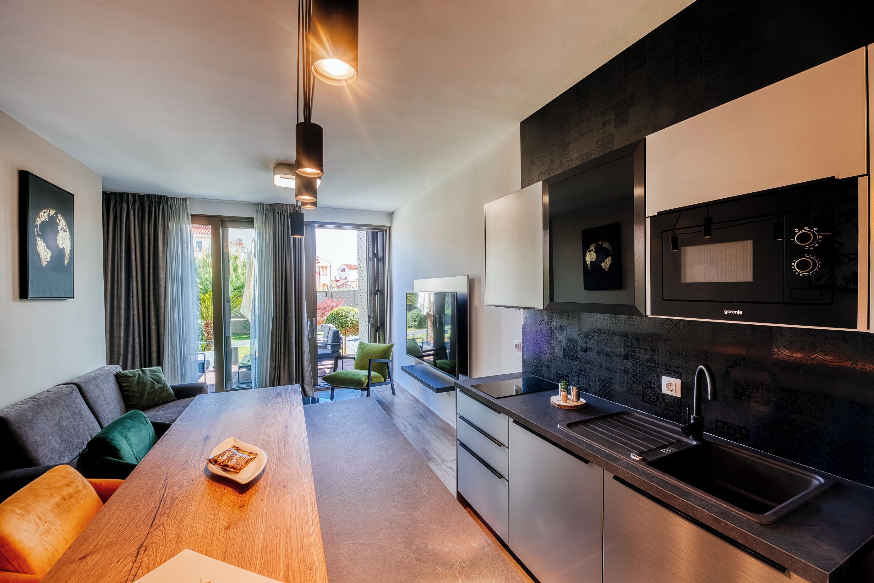 A modern kitchen with a microwave, sink, and dark cabinetry. There is a dining area with a wooden table and a sofa.