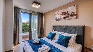 A hotel room with a bed, a painting on the wall, and a view of greenery outside.