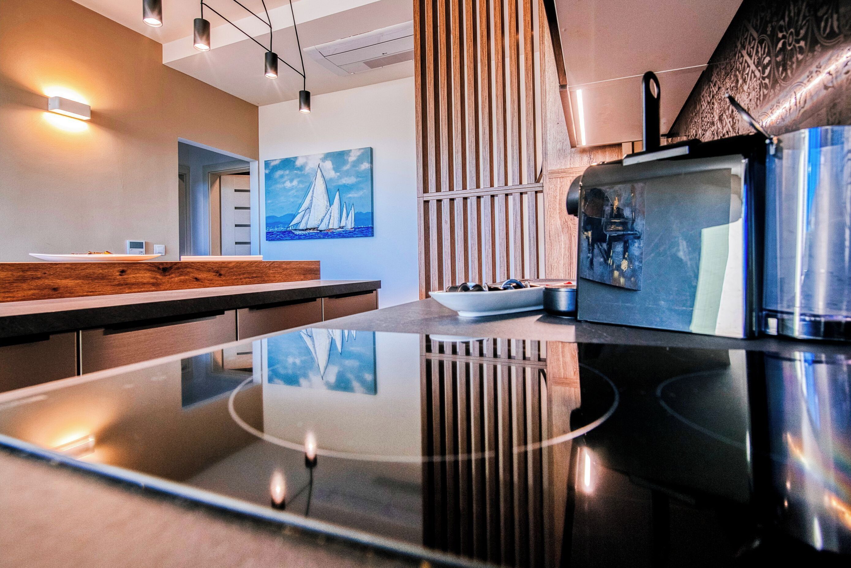 Une cuisine moderne avec un plan de travail en bois, une table à manger avec un plateau en verre et un réfrigérateur en acier inoxydable.