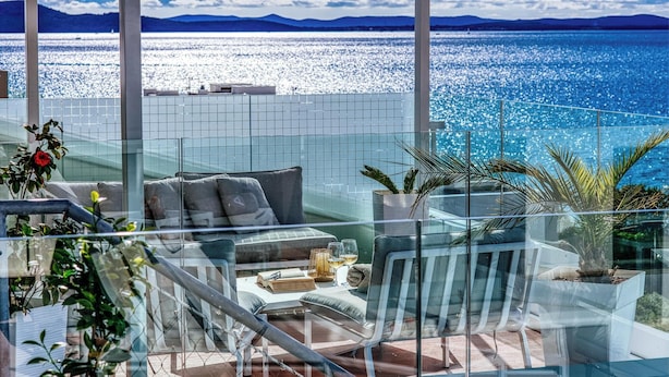 A balcony with a glass railing, a sofa, and a table with drinks and books.