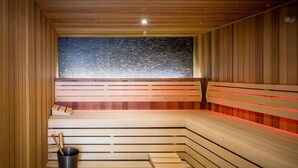 A sauna with wooden benches, a black bucket, and a textured wall. - Van Der Valk Hotel Deventer  (Deventer)