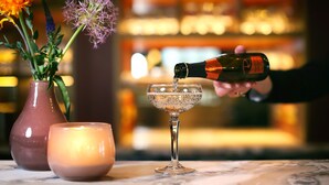 A bottle of champagne being poured into a glass on a marble surface, with a candle and a vase of flowers in the background. - Van Der Valk Hotel Deventer  (Deventer)