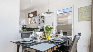 A modern dining area with a long table set for six, a kitchen in the background, and a balcony with a view. - Penthouse Sonnendeck 22 - Balcony, Barrel Sauna, Grill,Fireplace,Washing Machine (Olpenitz)