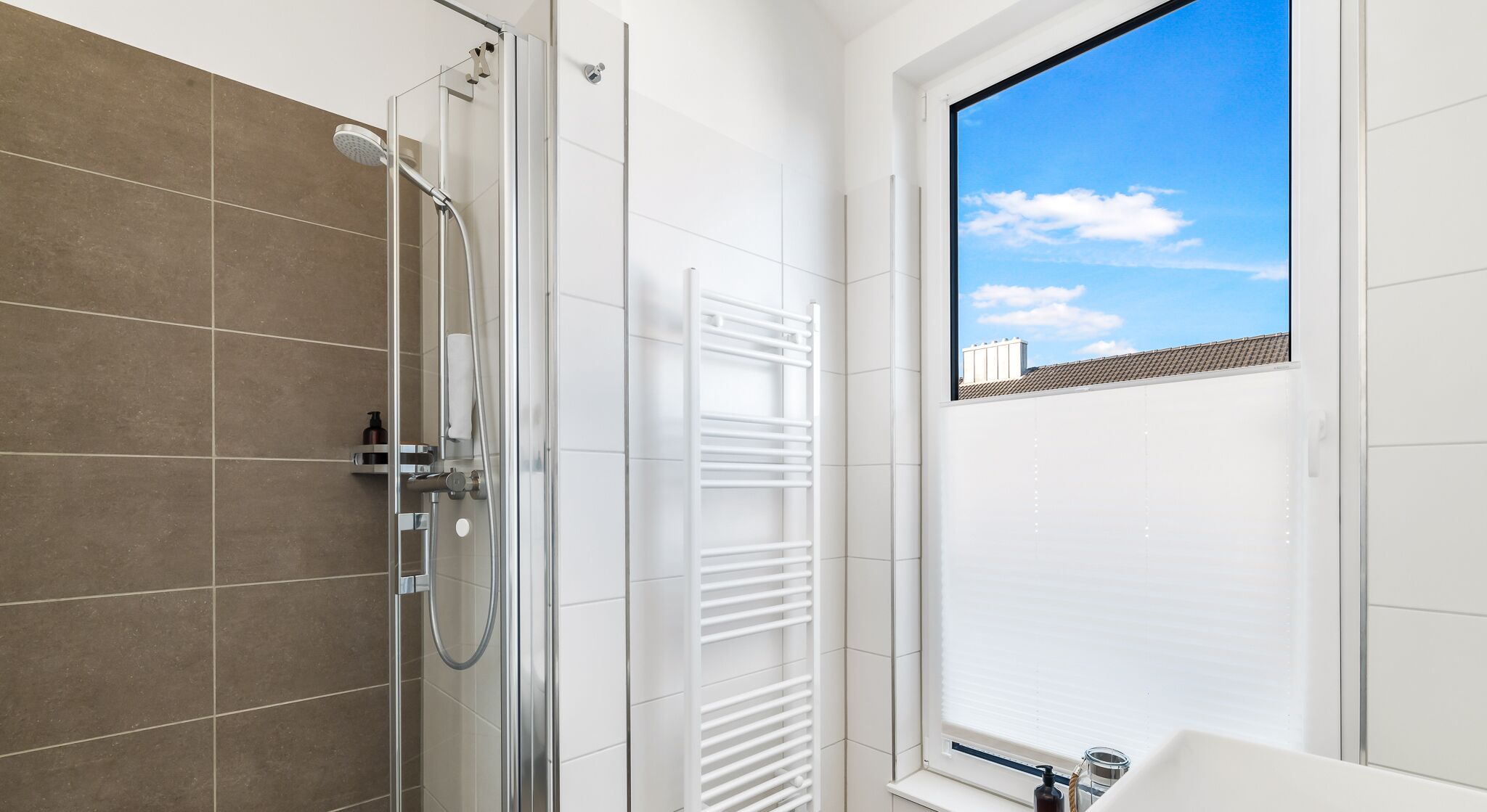 A modern bathroom with a glass shower enclosure, a white towel rack, and a view of the sky through a window.