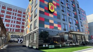 A multi-story hotel with a colorful facade, large windows, and a well-maintained lawn area. - Super 8 by Wyndham Brooklyn Williamsburg (Brooklyn)