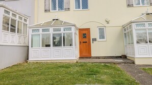 Une maison à deux étages avec une véranda, une porte d’entrée en bois et un petit jardin.