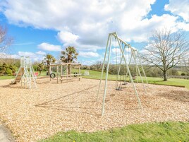A playground with swings and a slide, surrounded by a grassy area and trees.