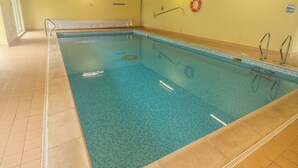 An indoor swimming pool with clear blue water, tiled floor, and a wooden ceiling. - Grooms Cottage (Tenby)