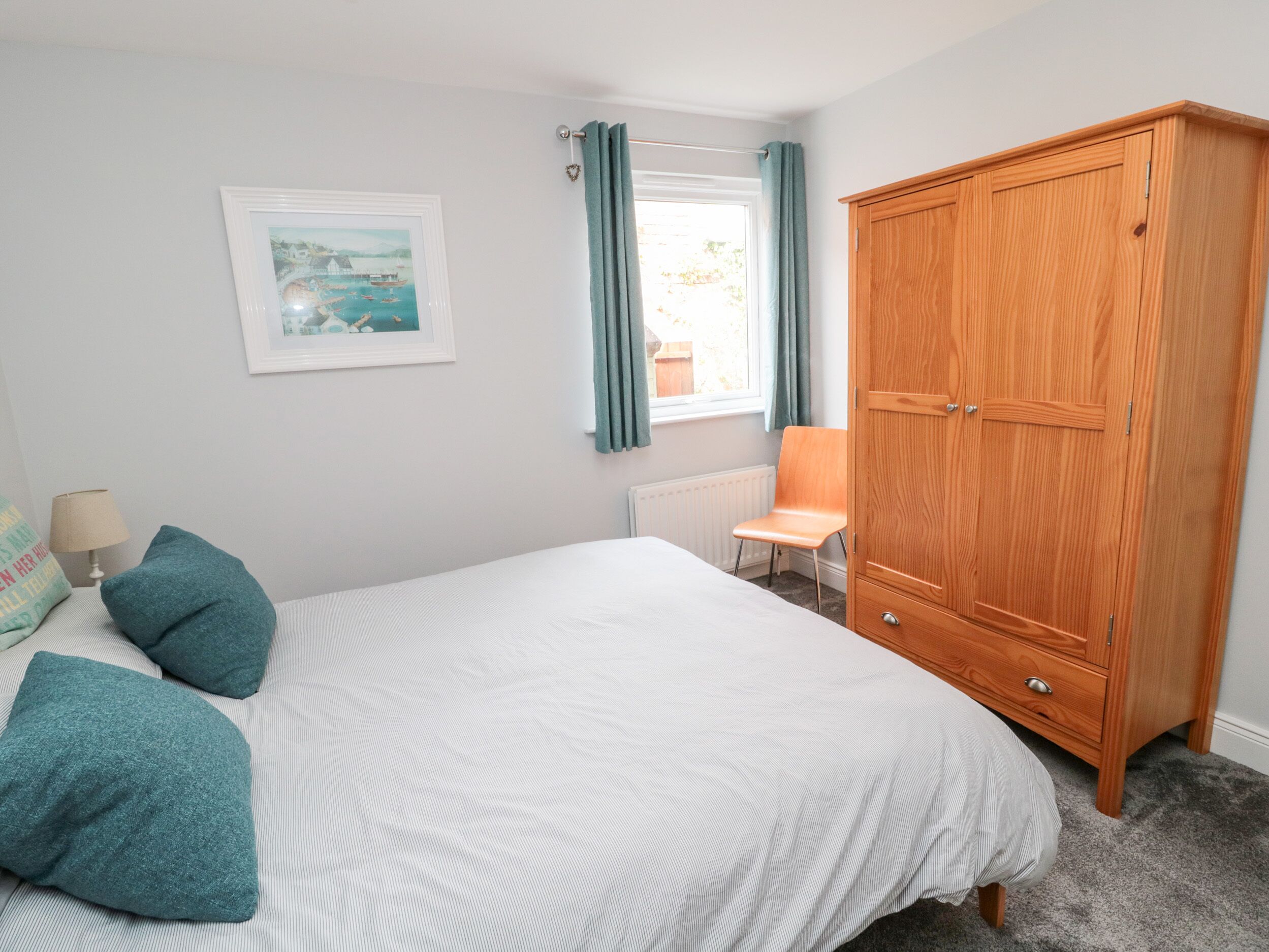 Une chambre à coucher avec un lit, une armoire en bois, une chaise, un radiateur et une fenêtre avec des rideaux.
