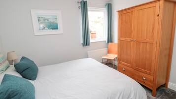 Une chambre à coucher avec un lit, une armoire en bois, une chaise, un radiateur et une fenêtre avec des rideaux.