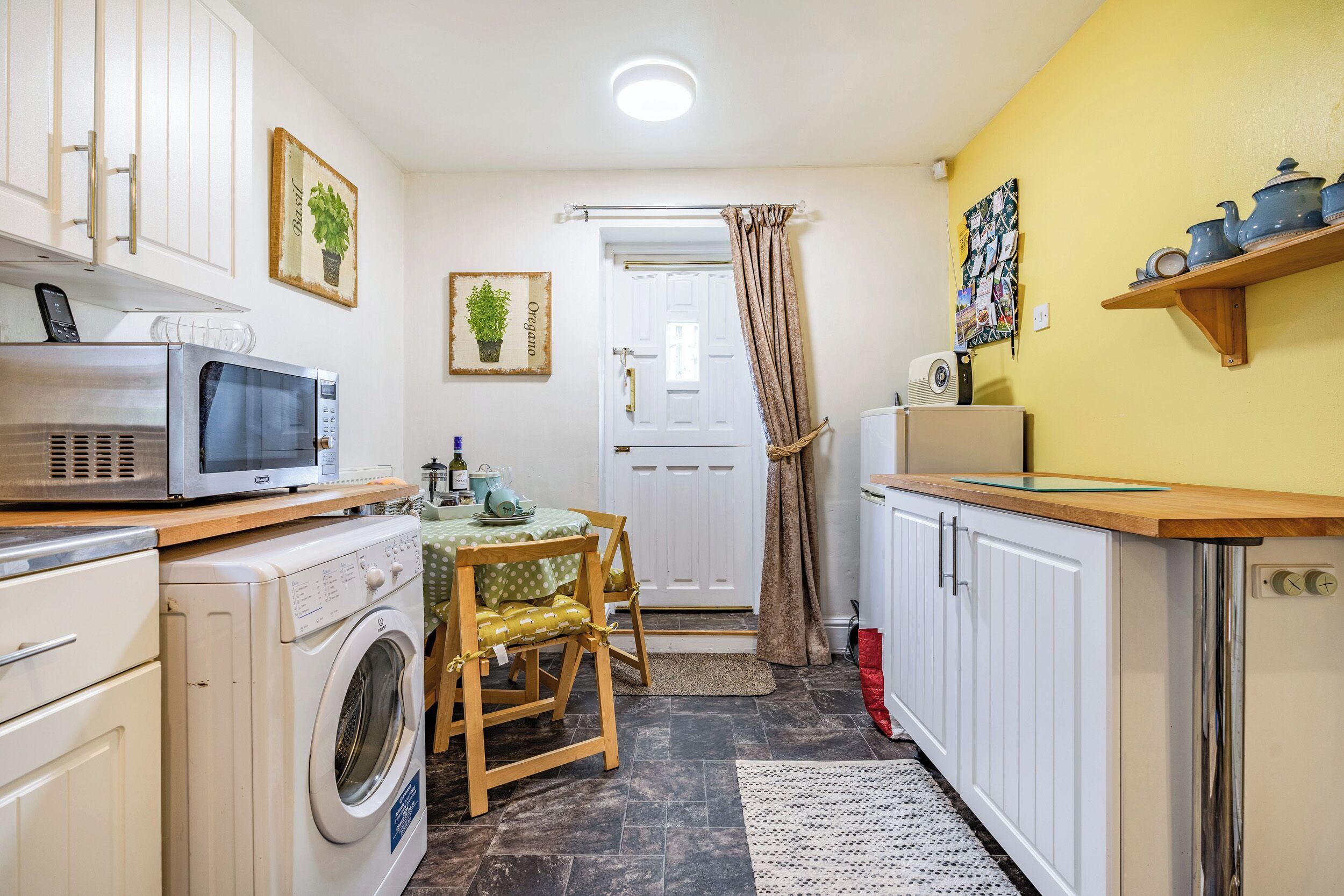 Une cuisine compacte équipée d’un lave-linge, d’un four à micro-ondes et d’un petit coin repas avec une table et une chaise.