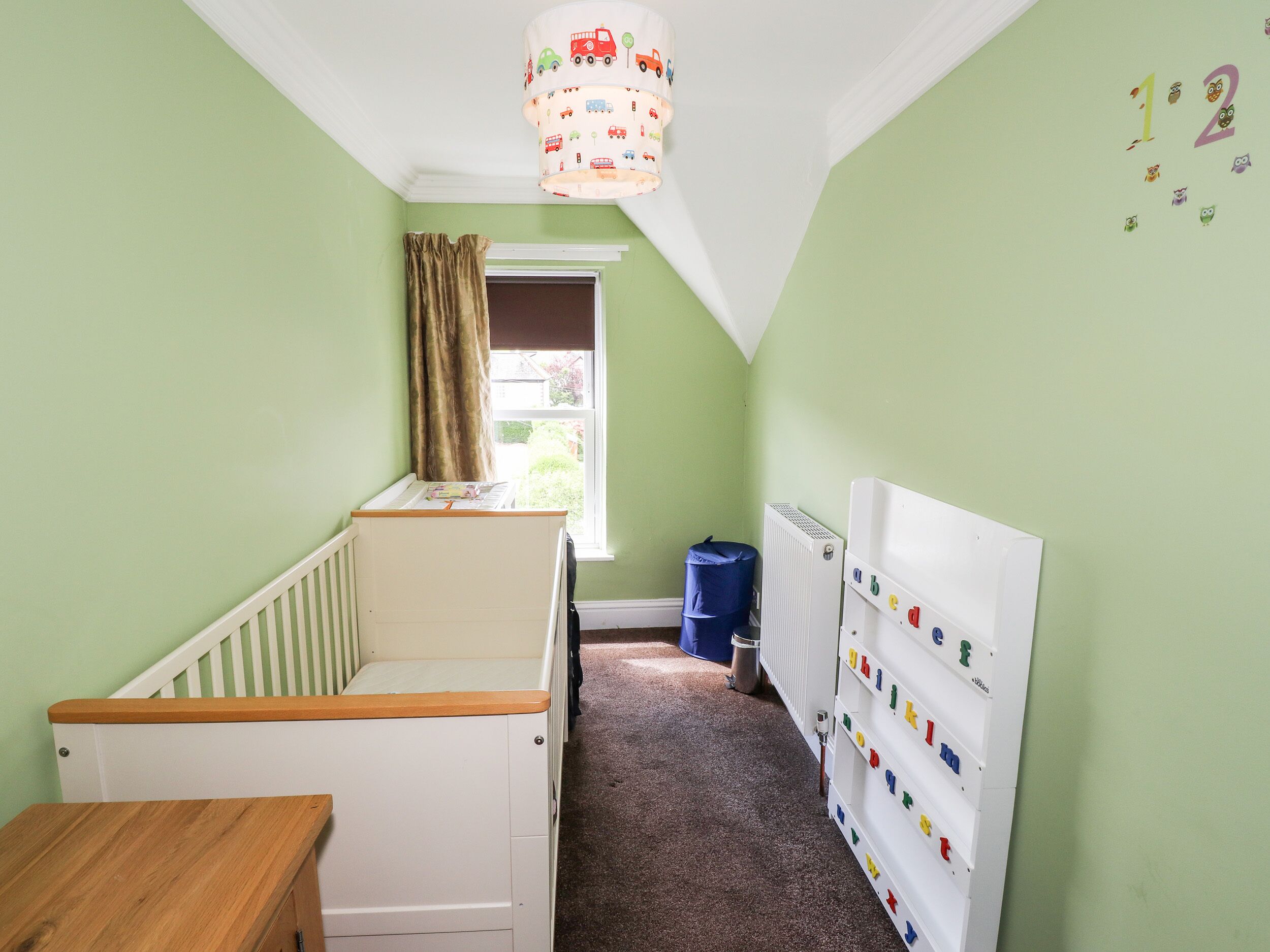 A child's room with a crib, a radiator, alphabet letters on the wall, and a window with curtains.